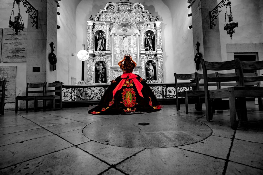 A dramatic red dress contrasts against a black and white church interior with ornate altar and religious statues.