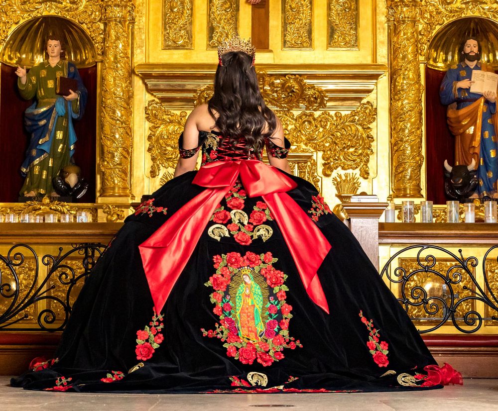 Ornate black and red quinceañera dresses with floral embroidery displayed against a golden baroque church backdrop.
