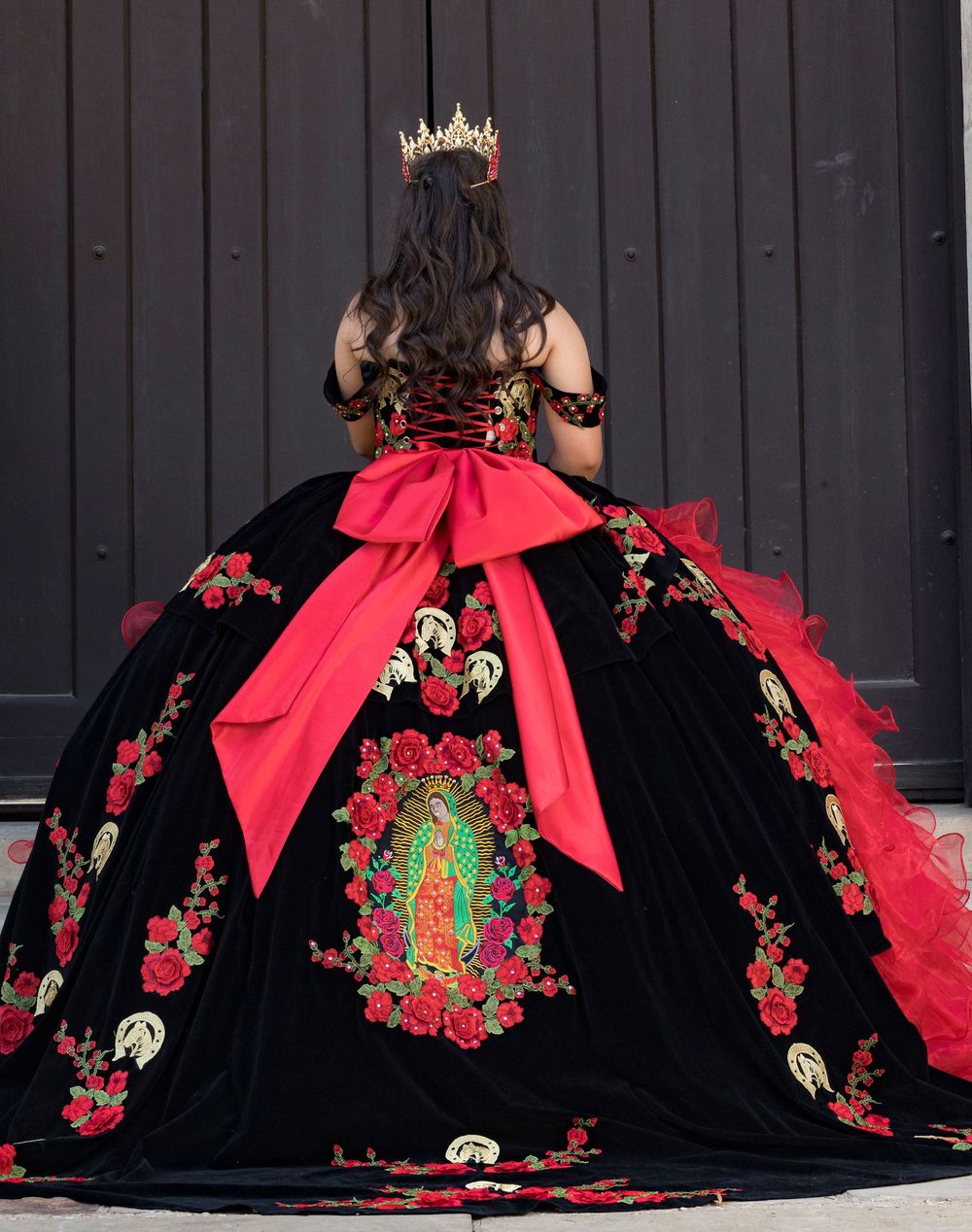 Dramatic black and red quinceañera dress with floral embroidery displayed against dark background.