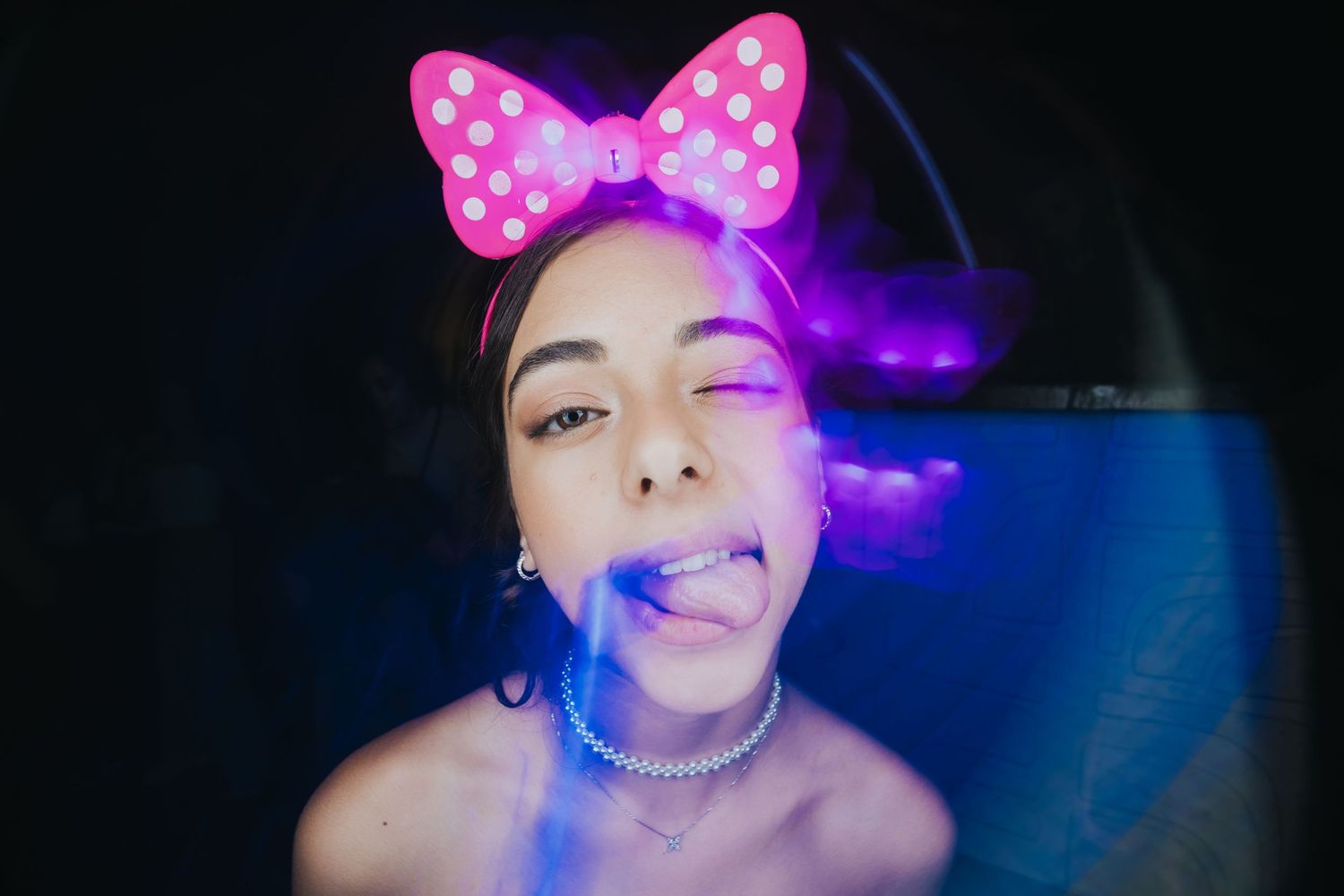 Creative portrait with pink bow and purple lighting effects on dark background.