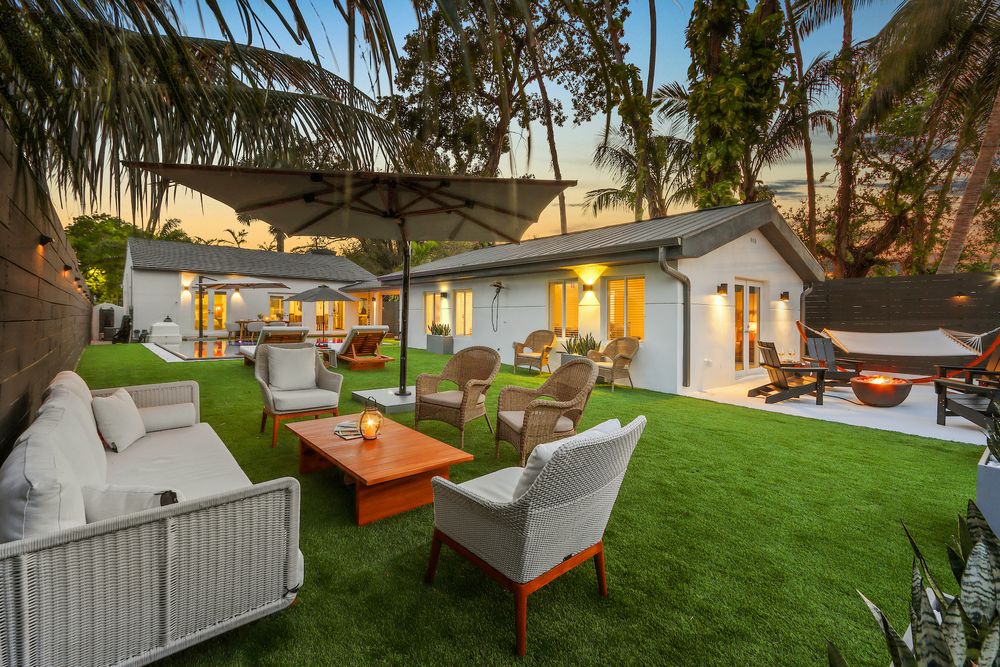 Modern backyard patio with artificial grass, comfortable outdoor furniture and warm lighting at twilight.