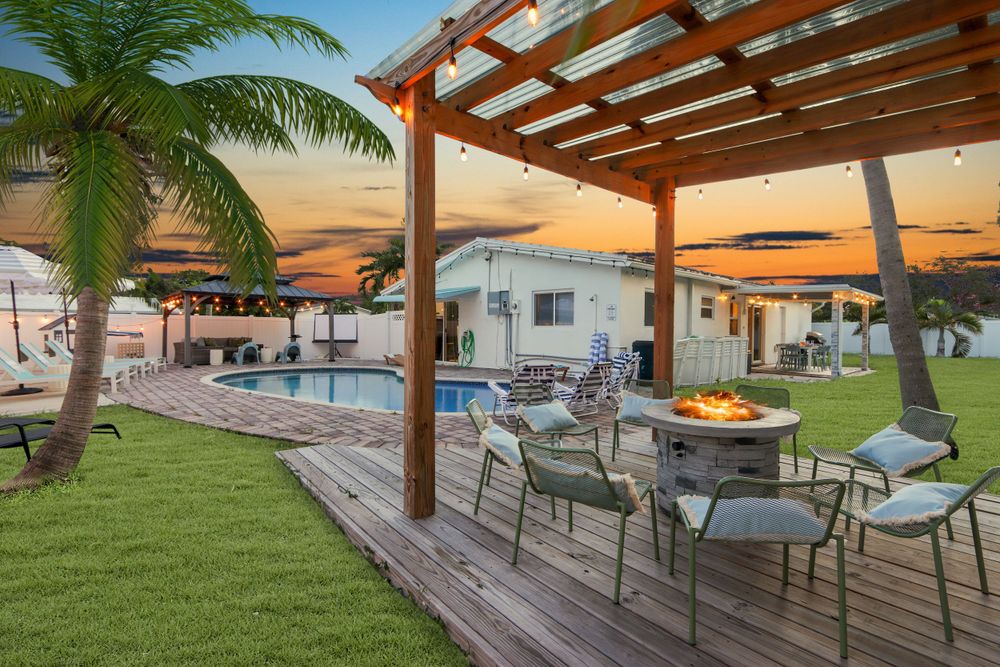 Modern backyard patio with wooden pergola, pool, and palm trees at sunset creating a resort-like ambiance.