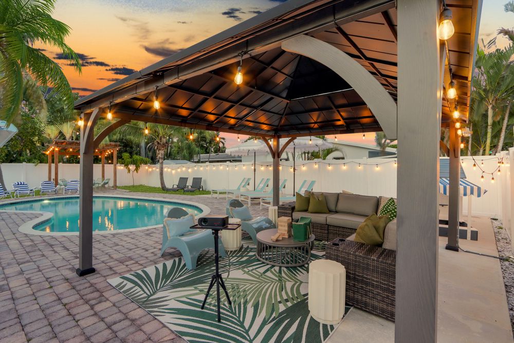 Luxurious backyard gazebo with string lights overlooking a swimming pool at sunset with tropical palm landscaping.