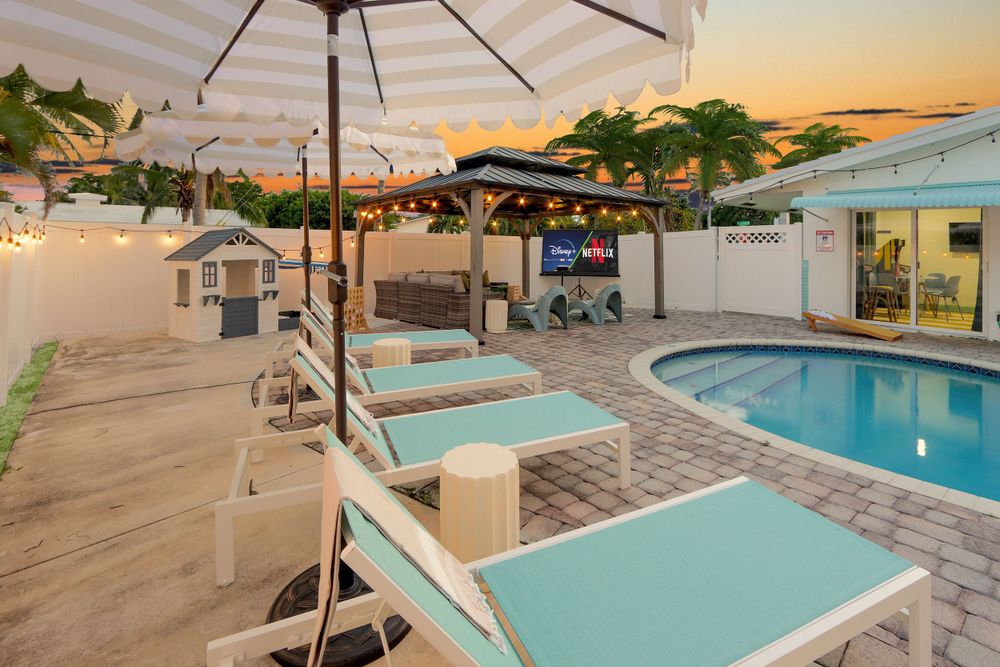 Pool loungers and umbrellas line a tranquil swimming pool at dusk with warm lighting and tropical landscaping.