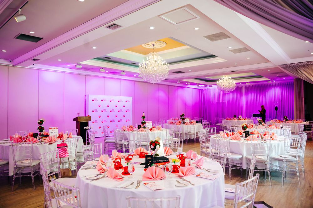 Elegant ballroom decorated in pink lighting with crystal chandeliers and round tables.