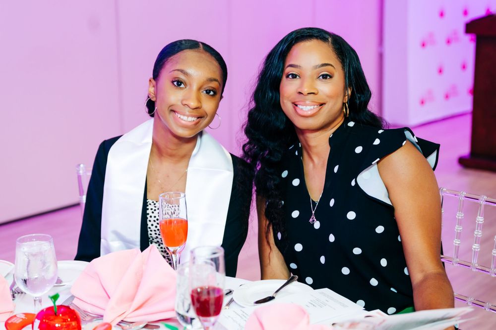 Women sharing smiles and conversations at an upscale social gathering with pink ambient lighting.
