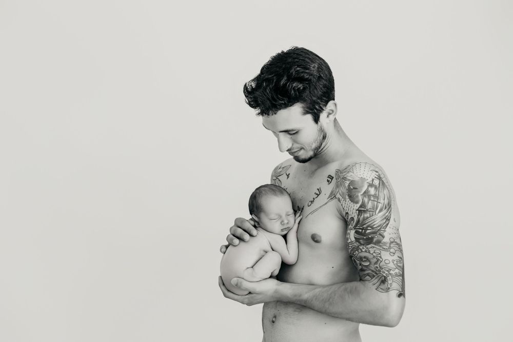 Fotografía en blanco y negro de padre mirando con amor a su hijo recién nacido en sus brazos.