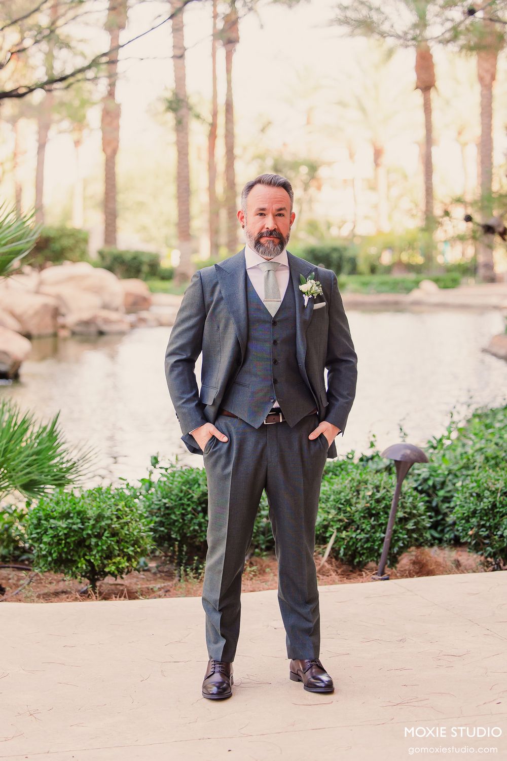 A series of four wedding photos showing someone in a charcoal gray suit and vest standing in a garden setting.