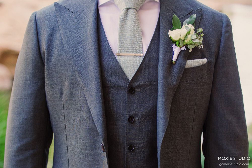 Detail shot of groomsmen wearing matching blue-gray suits with boutonnières lined up in a row.