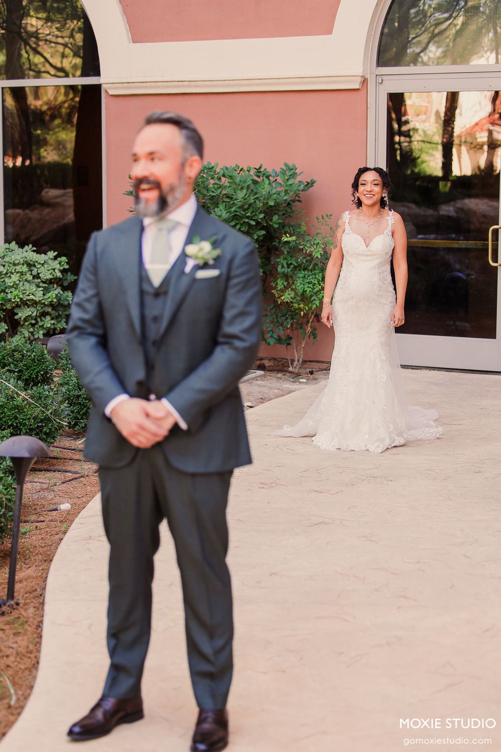 A couple shares a first look moment before their wedding ceremony outside a pink stucco building.