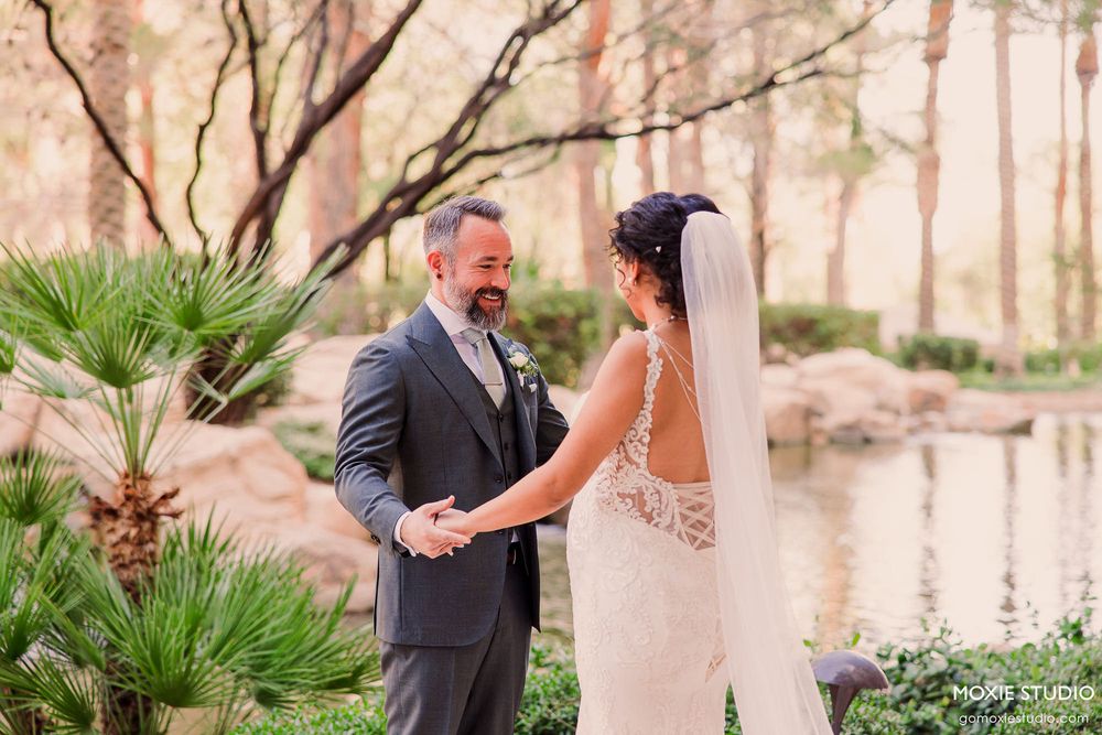 A couple in wedding attire shares romantic moments in a scenic outdoor garden setting with palm trees and natural light.