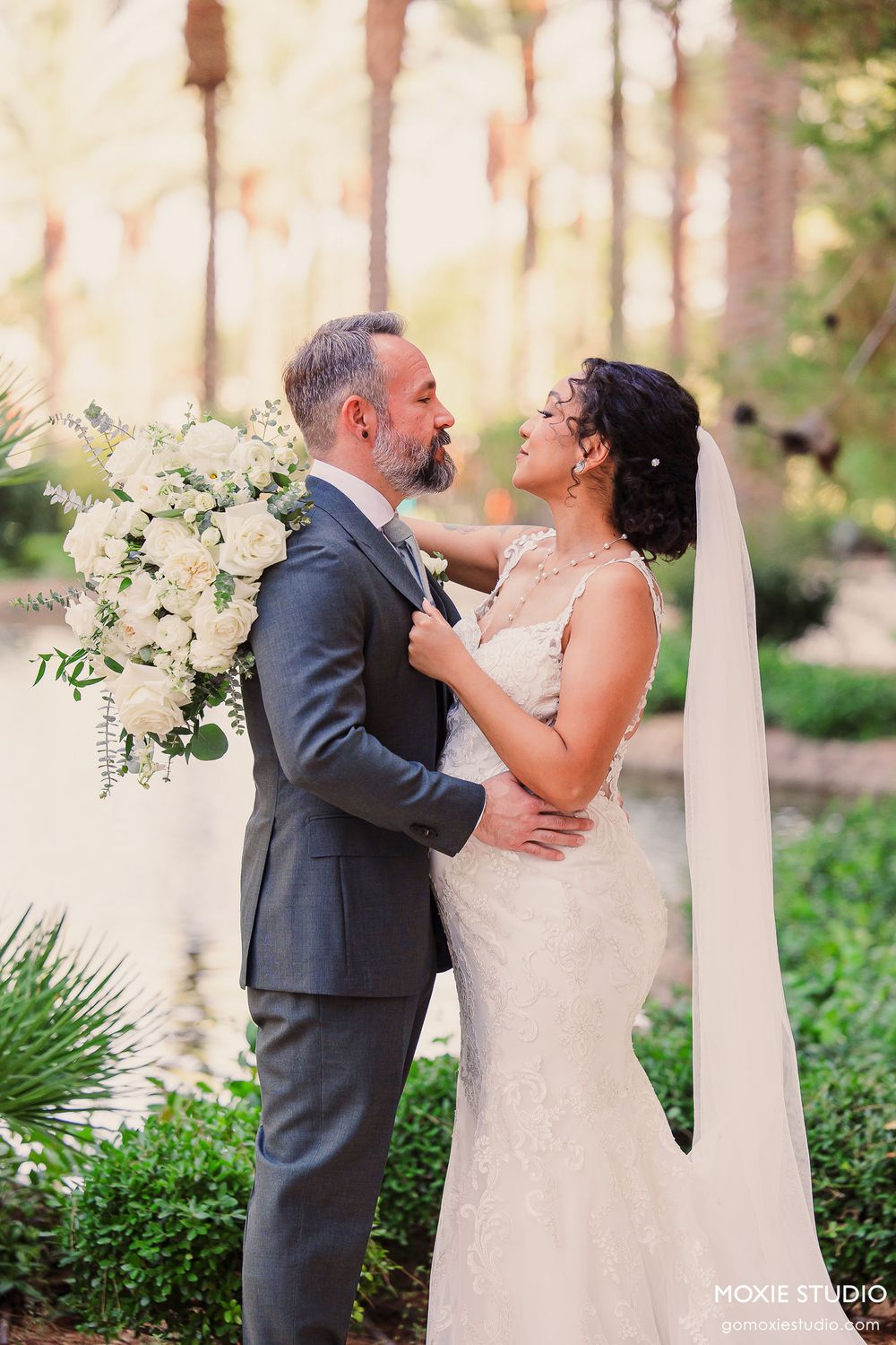 A couple shares a romantic moment during their outdoor wedding ceremony surrounded by greenery and white floral decor.