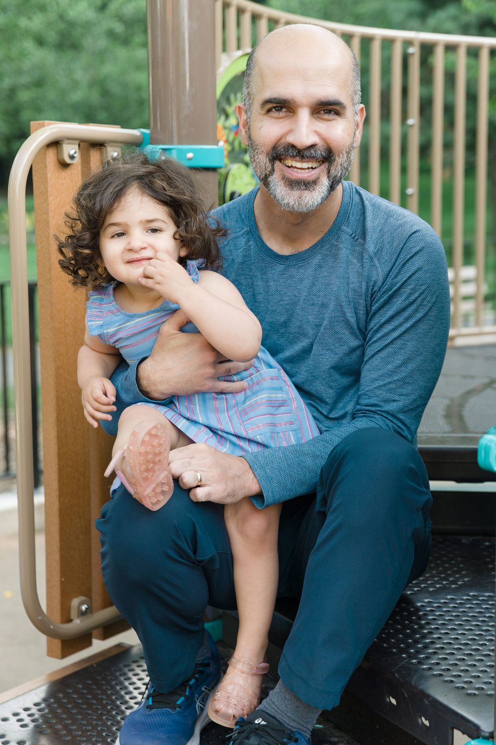 Adult and small child smile together while playing on outdoor playground equipment.