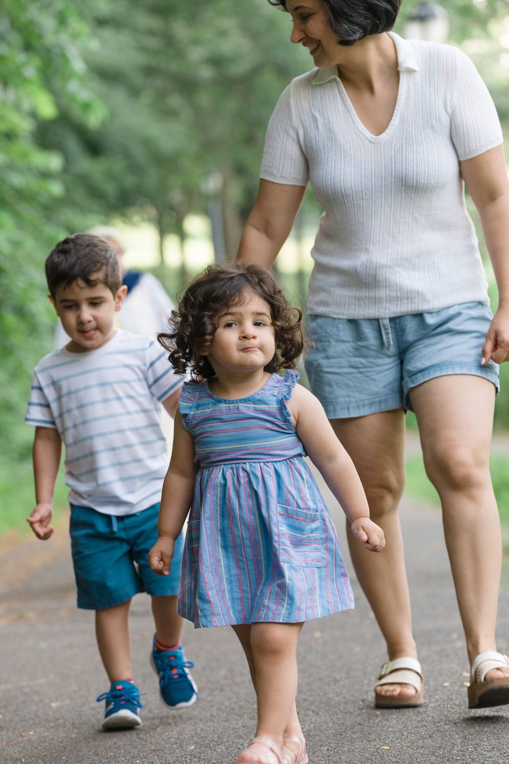 Side view of legs walking along a dirt path through greenery, showing adults and children moving together.