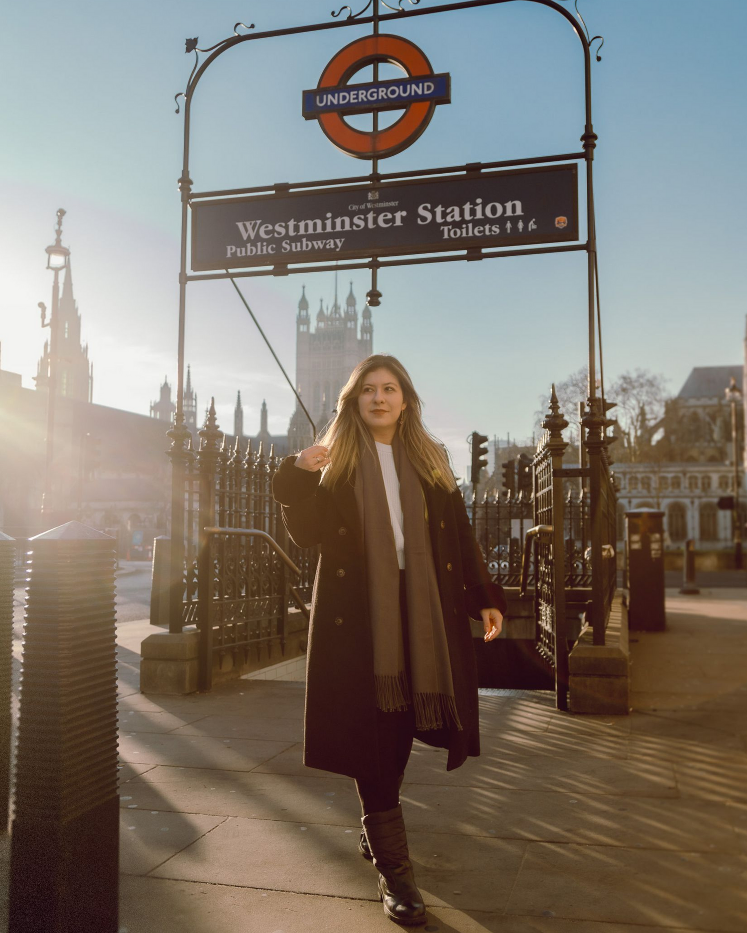 Person in long coat standing under Westminster Station sign in London.