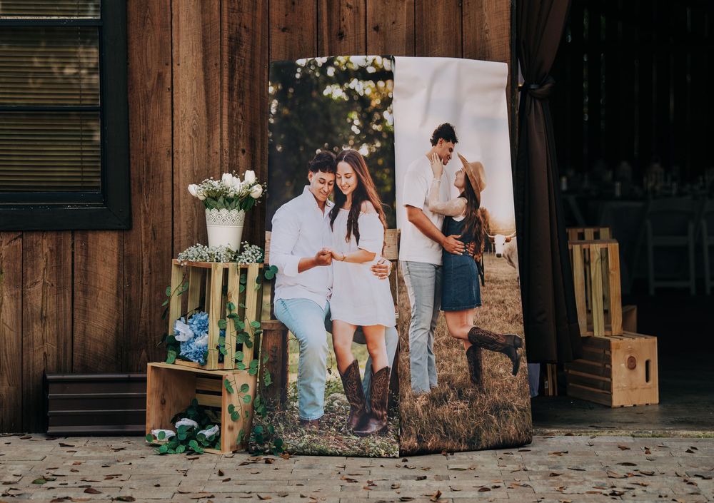 Large wedding photo banner displayed outdoors near a rustic barn, featuring a couple in casual attire with floral decor.