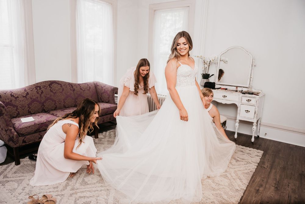 A wedding dress fitting scene in an elegant white room with vintage furniture.