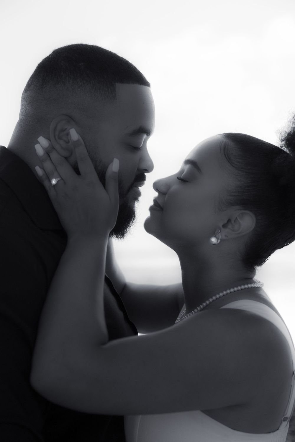Black and white photo of a romantic couple sharing an intimate moment, woman tenderly holding man's face.