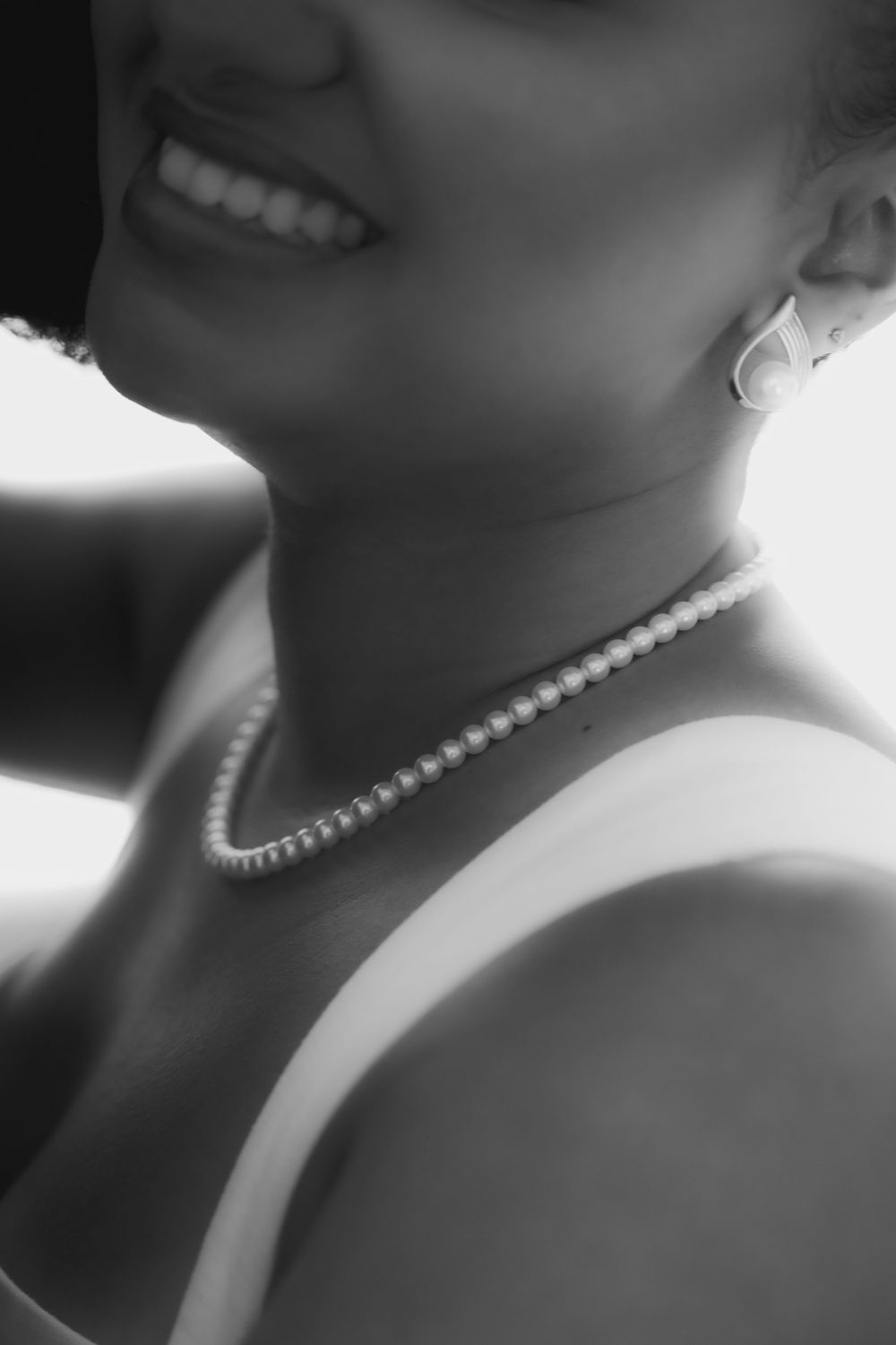 Black and white photo of a smiling woman wearing a pearl necklace and earrings in an elegant close-up portrait.