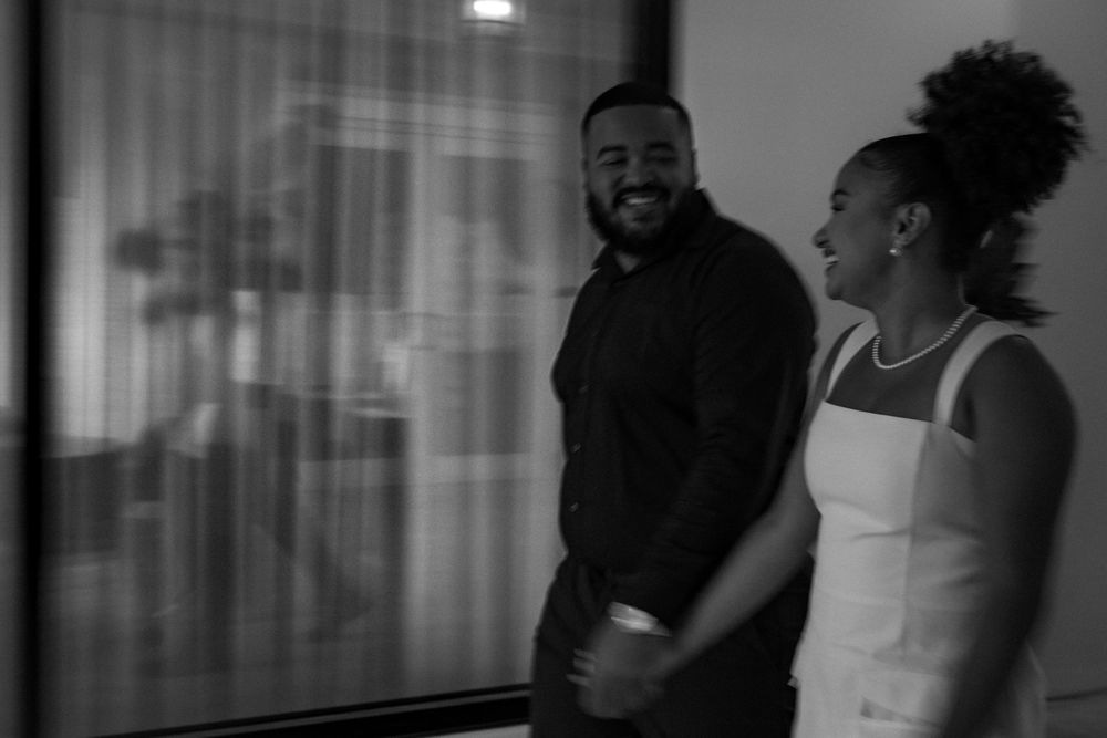 Black and white photo of a man and woman smiling and laughing together near a large window indoors.