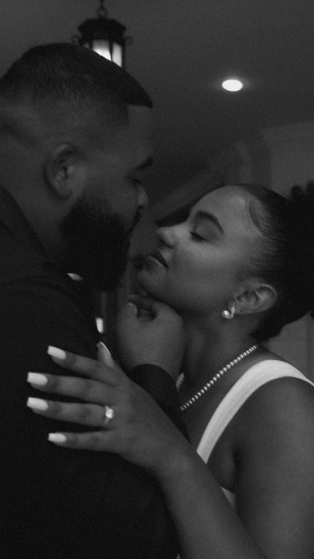 Black and white photo of a romantic couple sharing an intimate moment, woman wearing pearl necklace and white top.