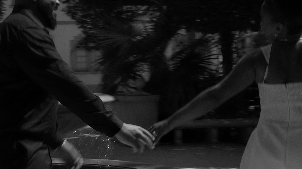 Black and white photo of two people holding hands near a car outdoors.