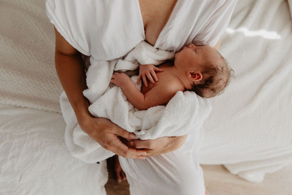 Un moment de tendresse entre parent et bébé alors qu’ils se tiennent la main alors qu’ils sont allongés ensemble sur une literie blanche.