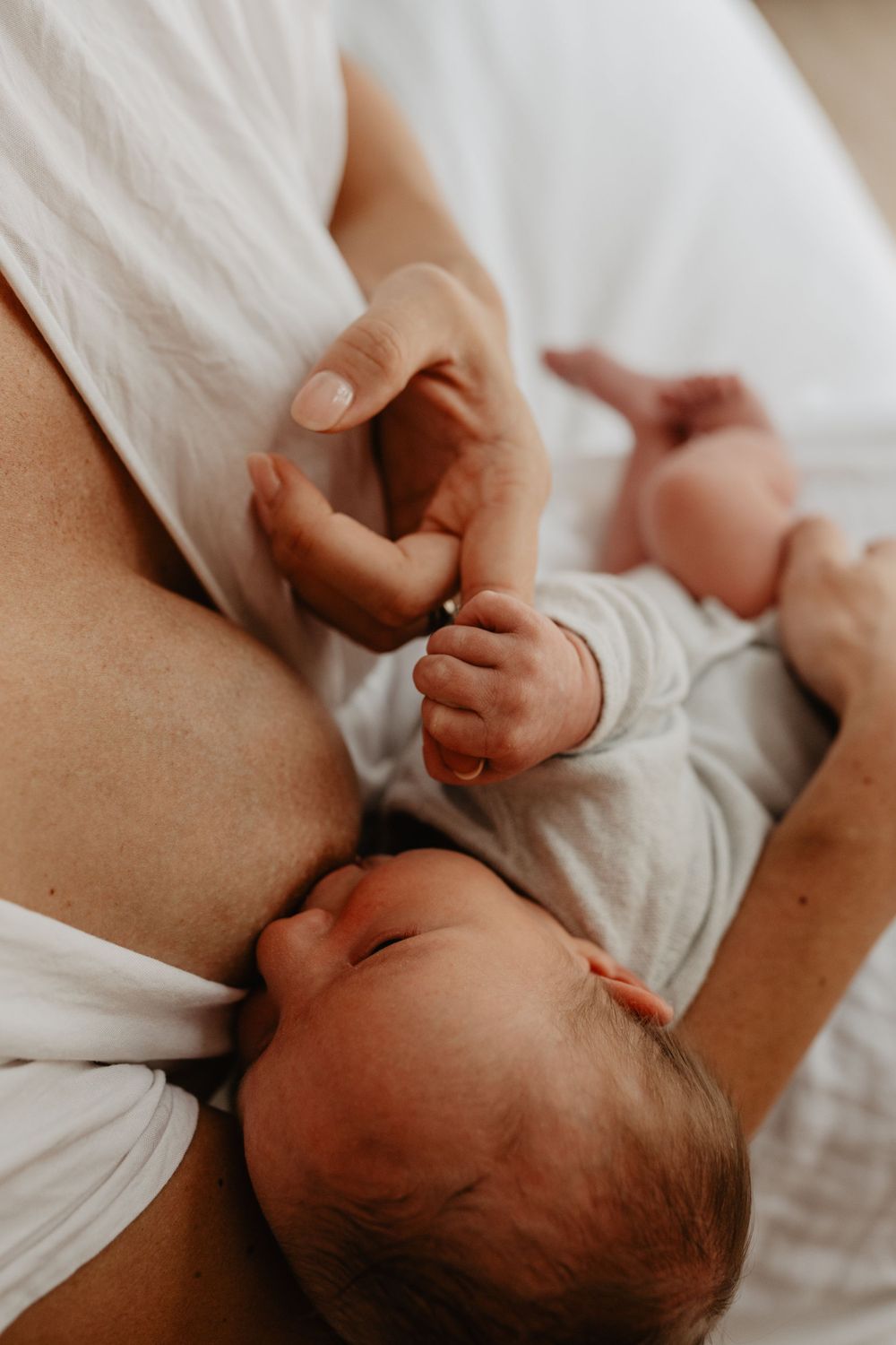 Un moment de tendresse entre parent et bébé alors qu’ils se tiennent la main alors qu’ils sont allongés ensemble sur une literie blanche.