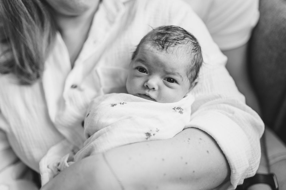 Un nouveau-né vêtu de blanc est tenu doucement dans les bras de ses parents