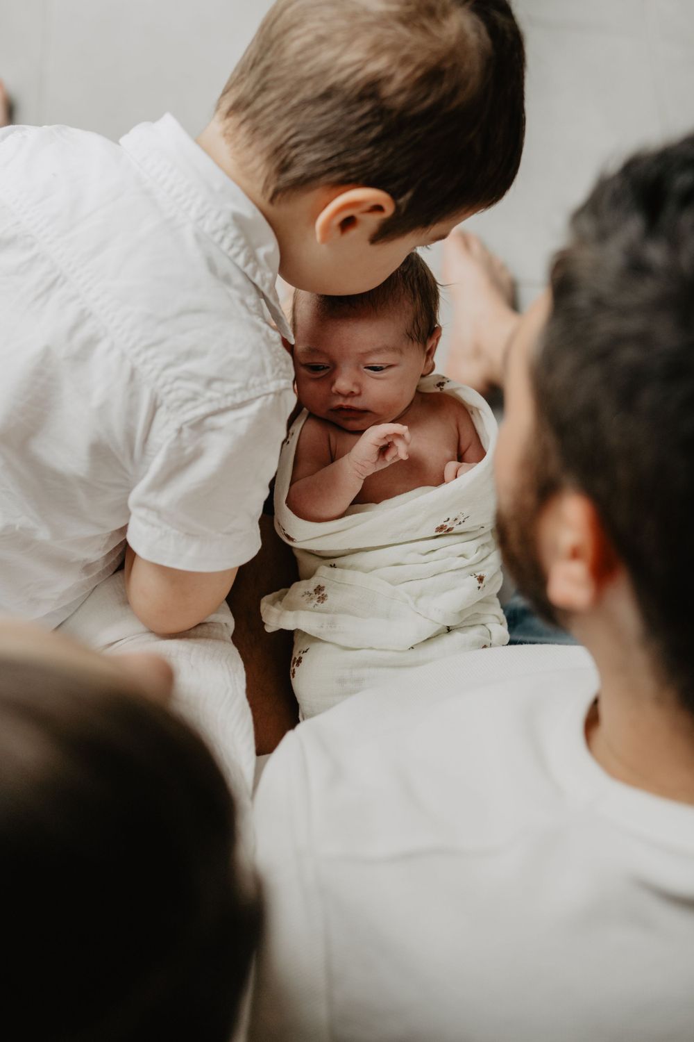 Un moment de tendresse montre un jeune enfant en blanc doucement penché sur un nouveau-né emmailloté.