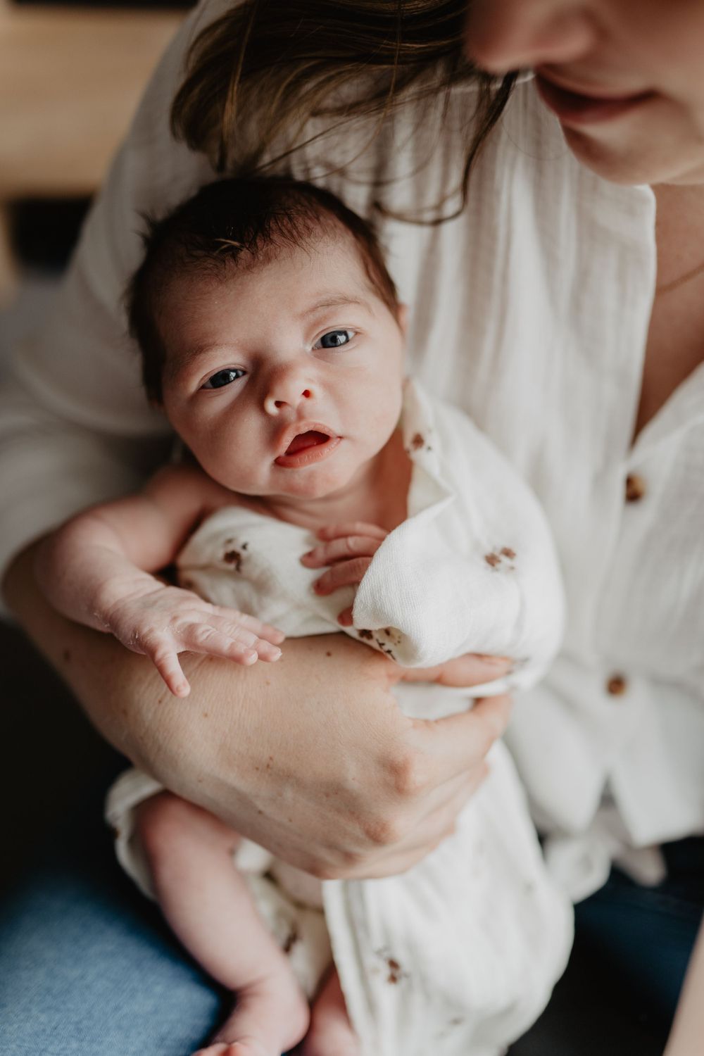 Un nouveau-né vêtu de blanc est tenu doucement dans les bras de ses parents