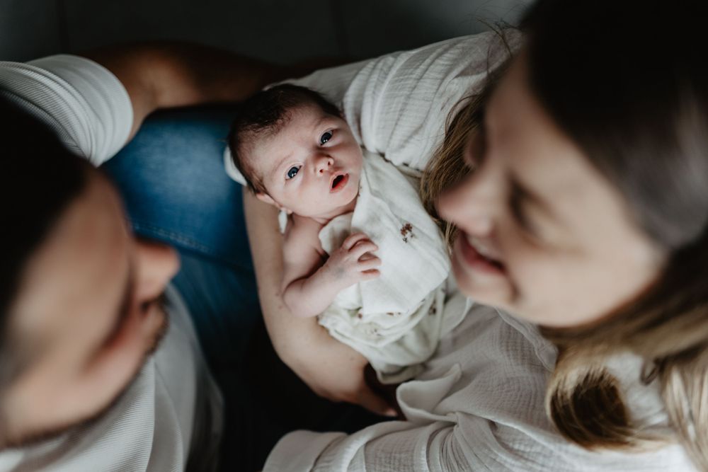 Un nouveau-né vêtu de blanc est tenu doucement dans les bras de ses parents