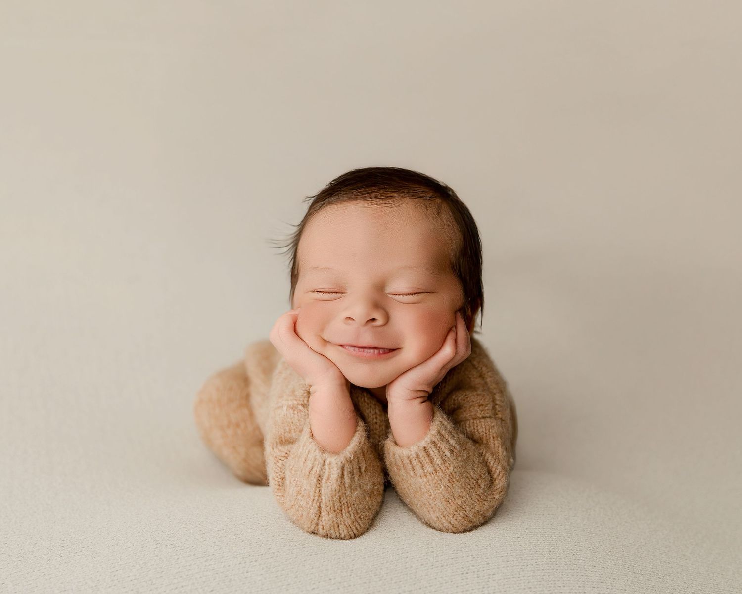 Sleeping newborn in delicate headband posed with hands under cheeks on gray backdrop.
