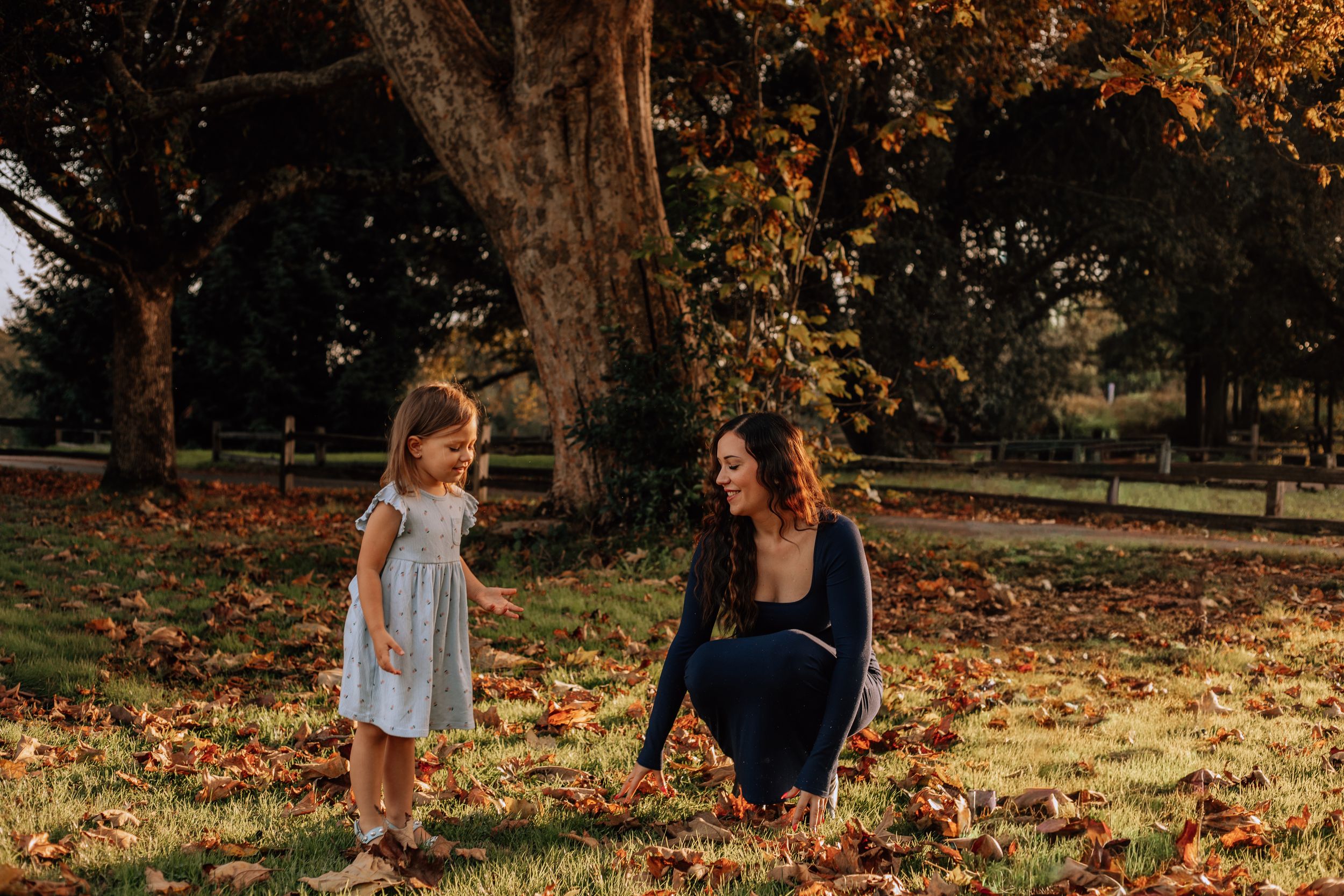 Children play in a pile of colorful autumn leaves during a fall photoshoot in a sunlit park.