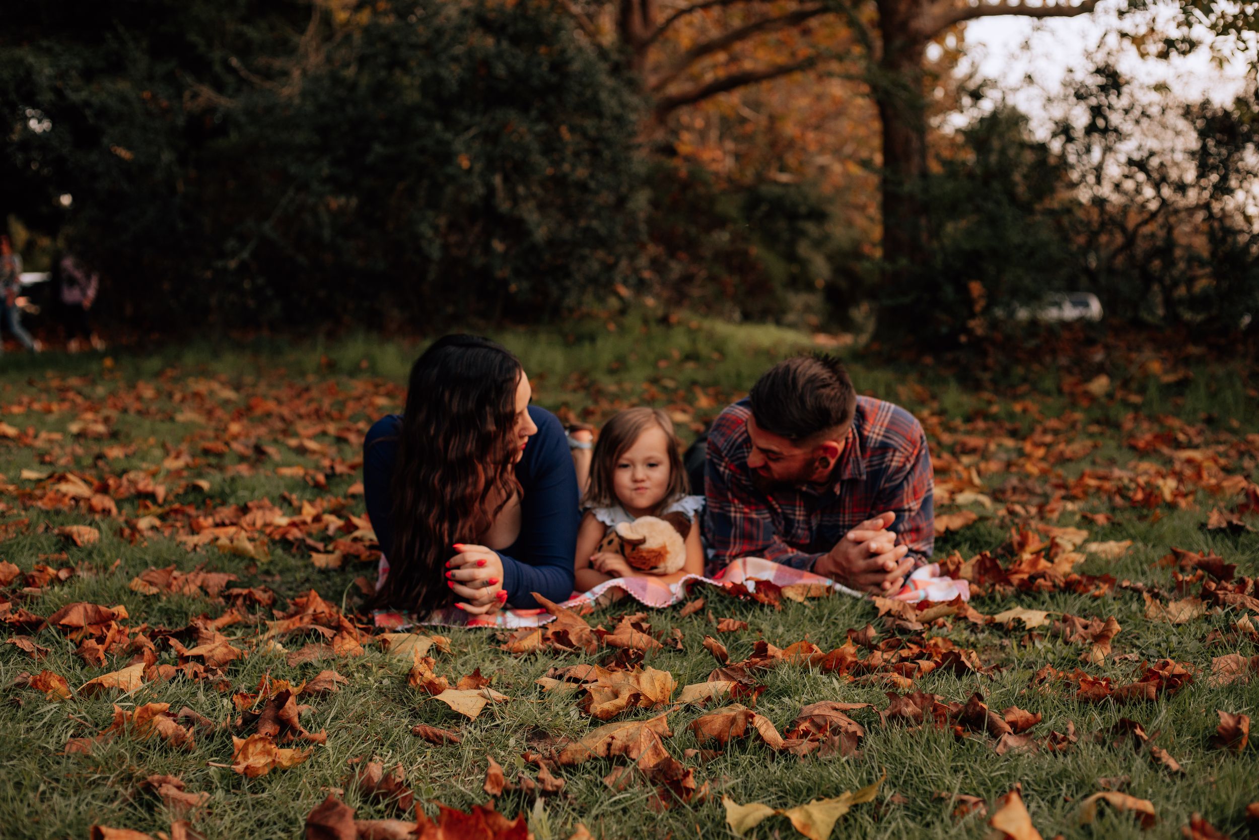 People lying on autumn leaves in a park during fall season with warm orange tones.