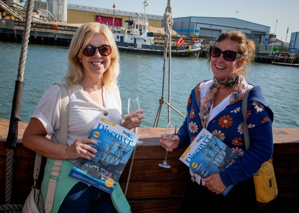 Two people enjoying drinks and holding books while sailing on a boat in a harbor.