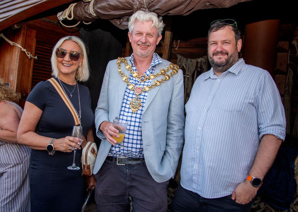 Three people stand together at an outdoor event with one wearing a chain of office decoration.