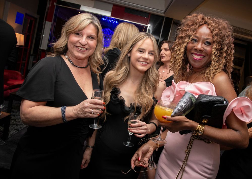 Three people enjoying drinks and socializing at a nightclub event with colorful lighting in the background.