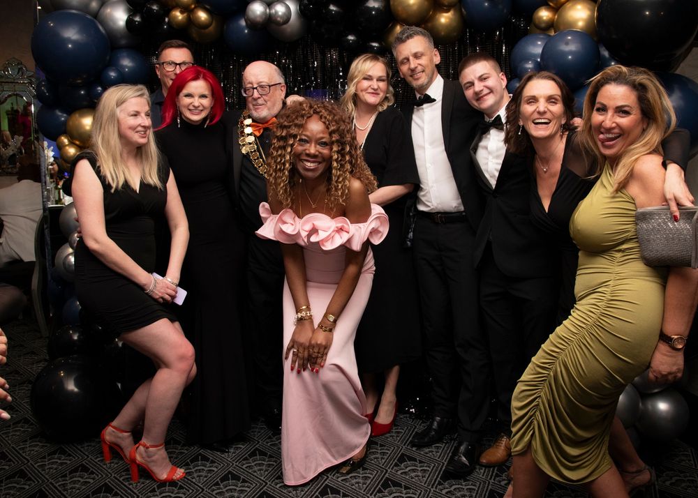 Party guests in formal wear posing together against a backdrop of black balloons at an elegant celebration.
