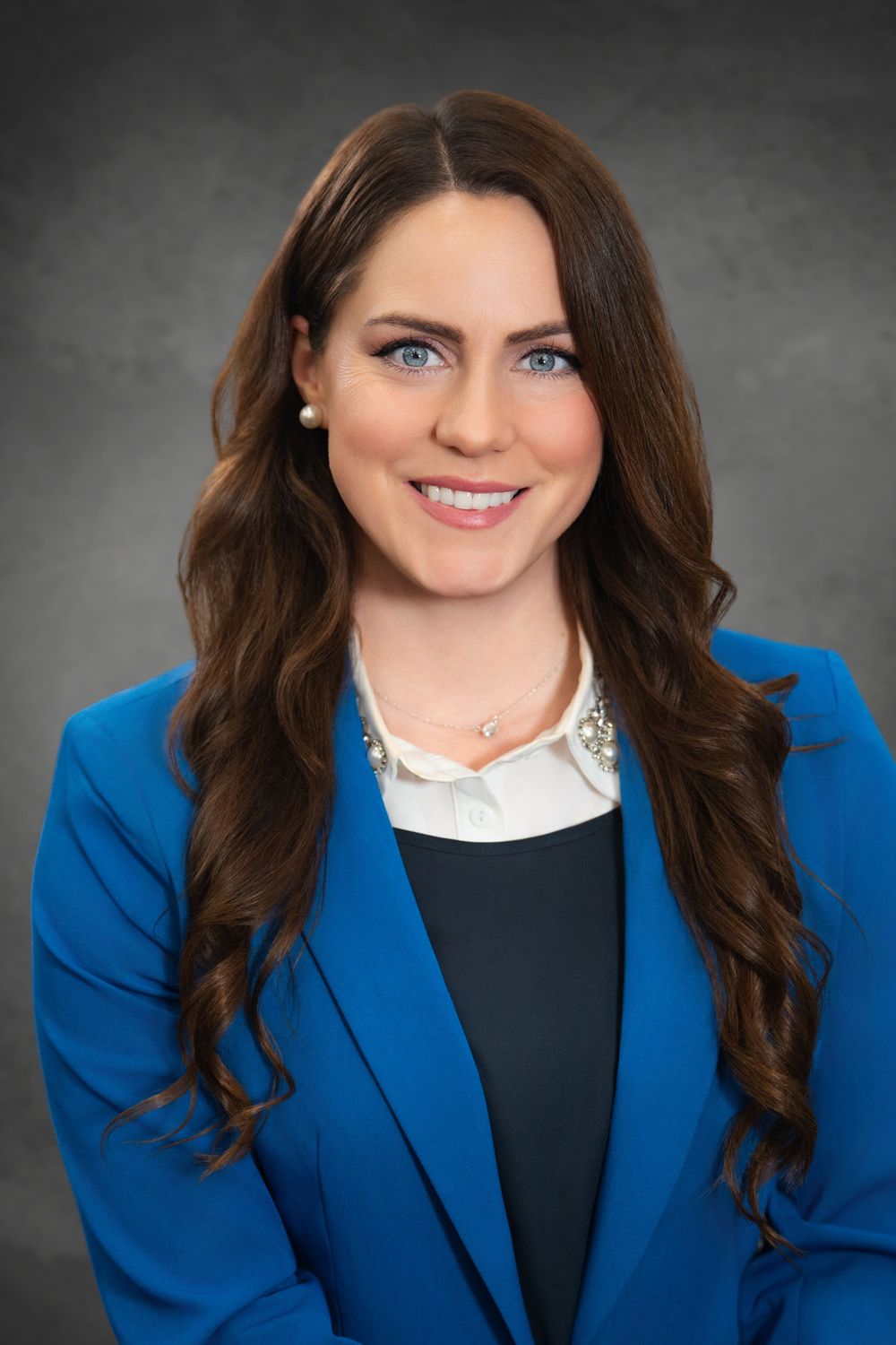 Professional headshot of a smiling woman with long brown hair wearing a blue blazer and white blouse.