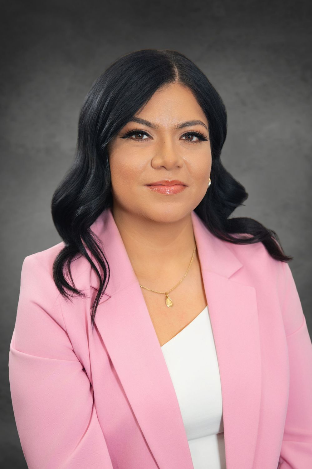 Professional woman in pink blazer and white top with gold necklace, posing for a formal business portrait.