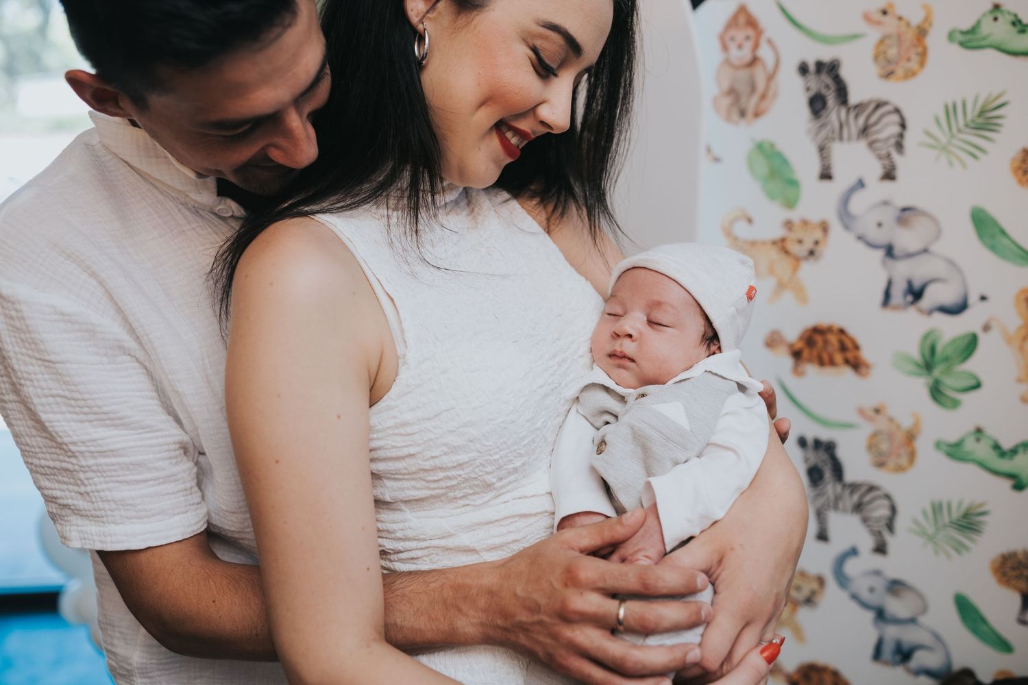 Family moment with newborn baby against a nursery wall with animal illustrations.