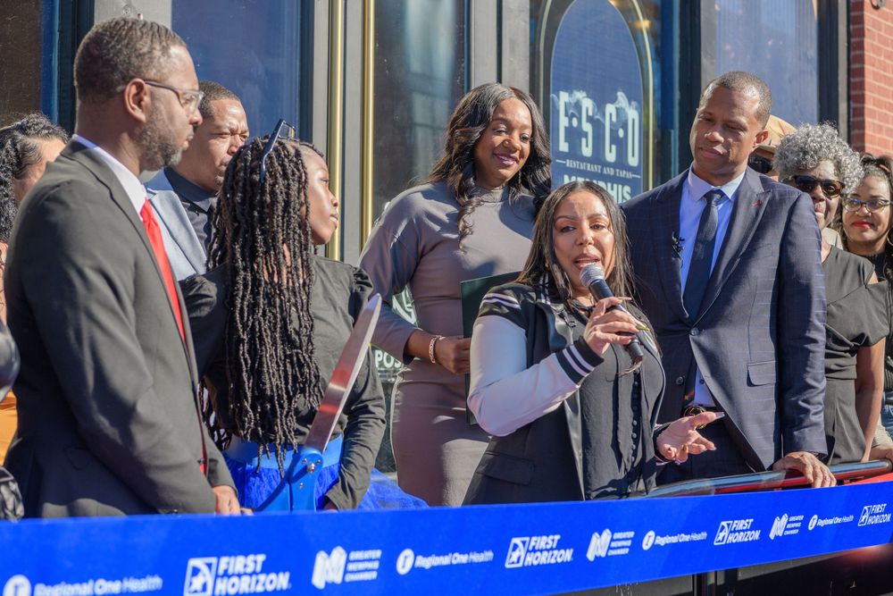 A group of people in business attire gather to participate in a ceremonial ribbon cutting event.