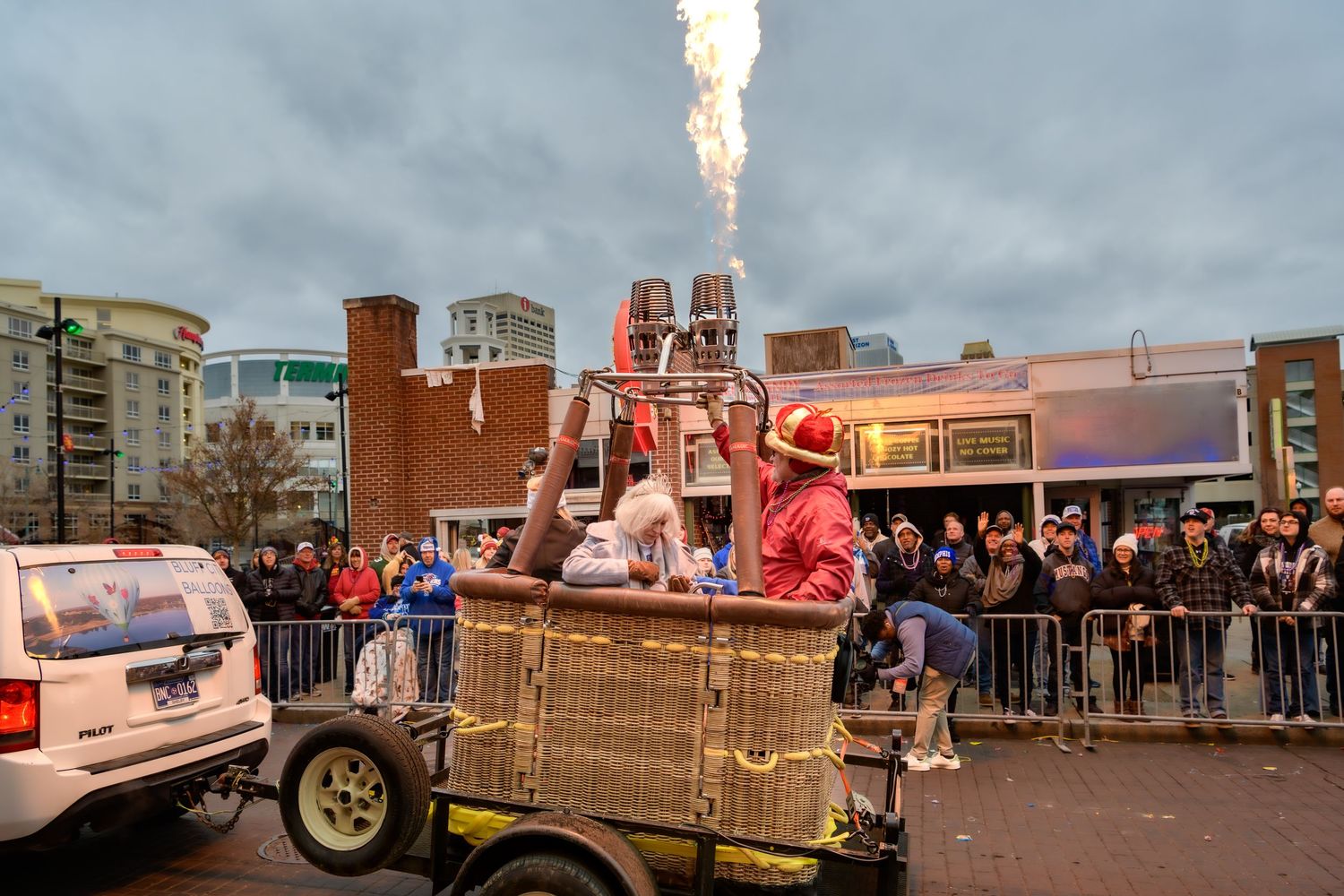 A festive crowd gathers around a steampunk-themed mobile cart with steam rising during an outdoor street event.
