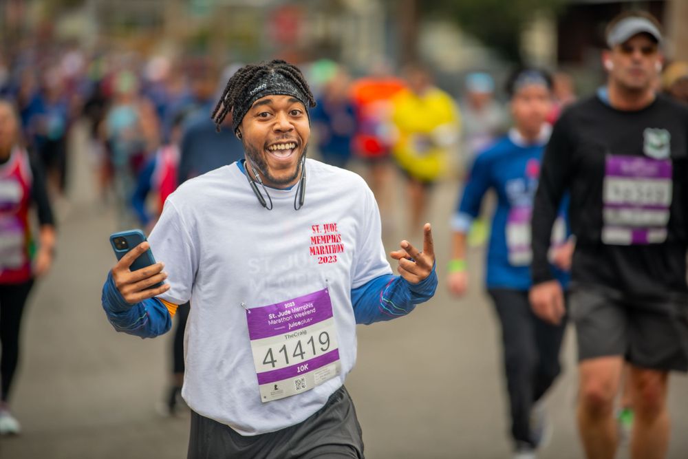 Happy marathon runner checks smartphone while jogging during a race event on city street.