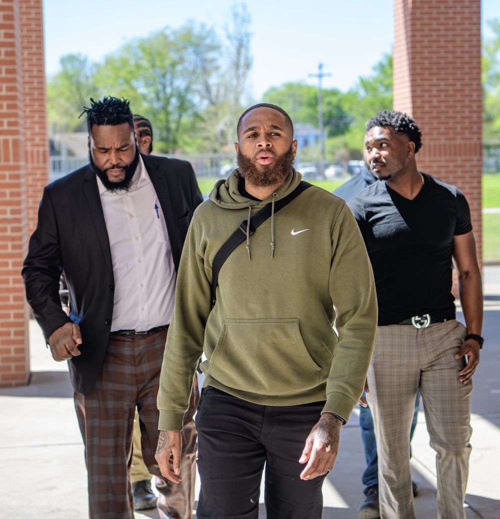 Three people walking together through a brick column entrance wearing casual attire including a Nike hoodie.
