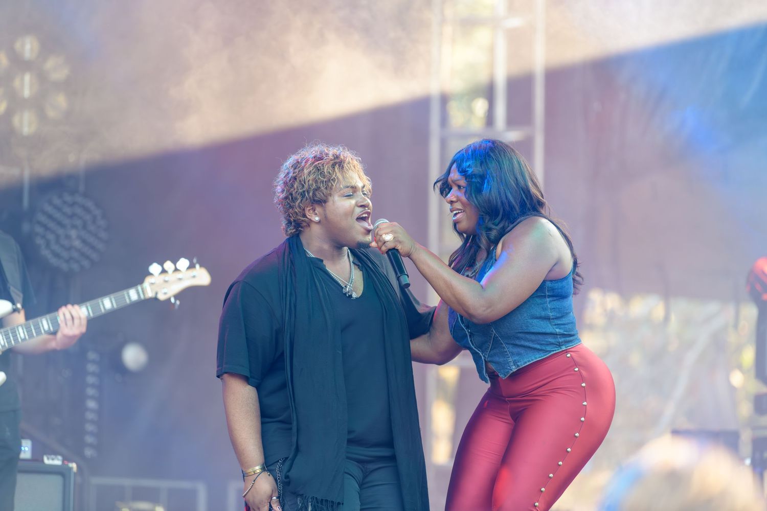 Two performers share an energetic moment on stage during a concert performance with dramatic lighting.