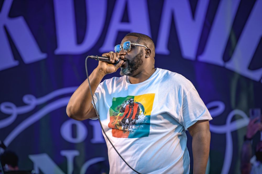 Performer wearing a light blue t-shirt with colorful graphic sings into microphone on stage with blue lighting behind them.