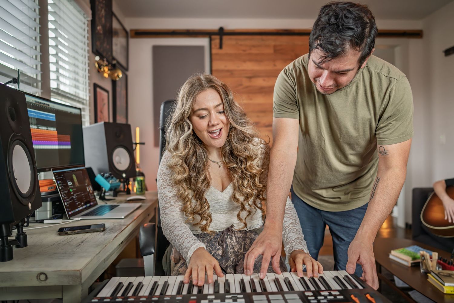 Two people enjoying playing music together on a keyboard in a home studio setting.