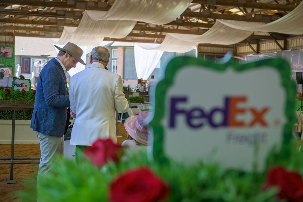 Business meeting scene at event with FedEx logo visible through blurred red flowers in foreground.